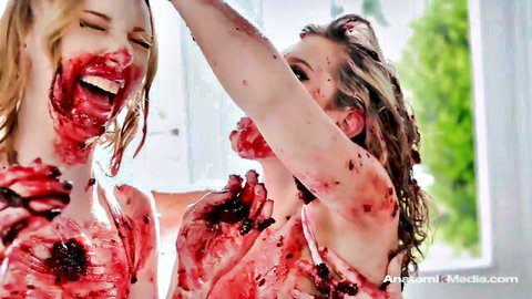 Two blonde girls laughing while covered in red pie mess in lingerie