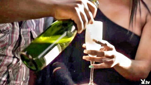 Voluptuous ebony woman in sexy black dress holding glass as man pours champagne