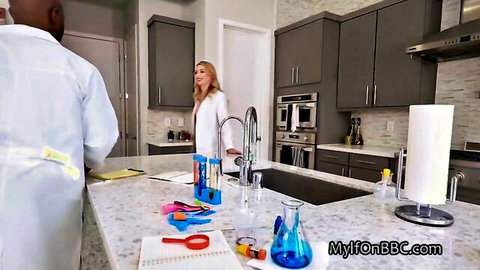Blonde white MILF in lab coat stands at kitchen counter with BBC black stud in white coat and science props.
