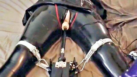 Bound woman in black latex with strap restraints and dildo insertion toy