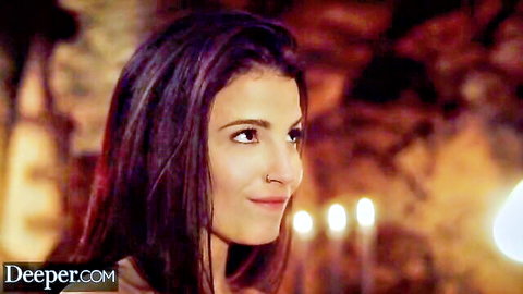 Busty MILF with long dark hair smiles seductively in candlelit scene