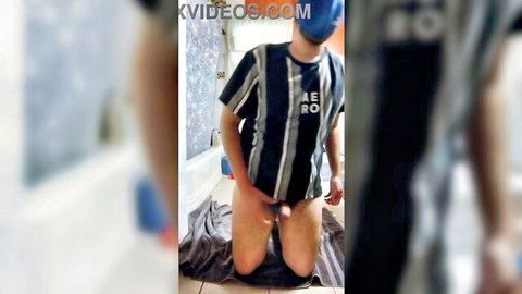Sissy kneels in bathroom pulling blue panties aside exposing cock and balls