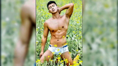 Muscular Asian male model flexing shirtless in white briefs amid yellow flowers