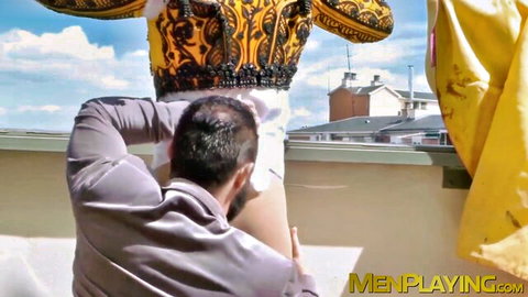 Hooded man grips ornate gold-costumed guy's bare ass for outdoor rooftop doggy style anal fuck