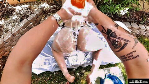 Tattooed hands pour thick white lube on girl's spread ass and pussy outdoors