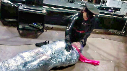 Goddess Nemesis in leather dominating mummified redhead slut