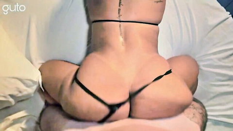 Tattooed big ass babe in tiny black thong sits on guy's lap from behind