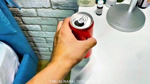 Hand gripping red soda can on white table with bottles and blue curtain
