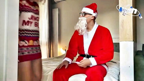 Woman in festive Christmas sweater teases Santa Claus in red suit on bed for holiday fun