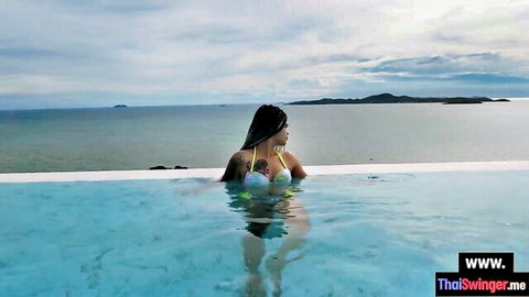 Asian teen in bikini poses seductively in pool by the sea