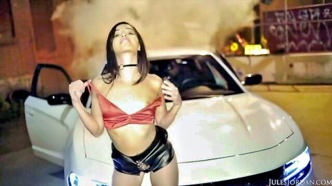 Emily Willis in red crop top and black shorts, seductive pose by white car at night