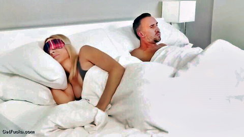 Blonde with sleep mask and big tits beside bearded man in bed, teasing couple scene