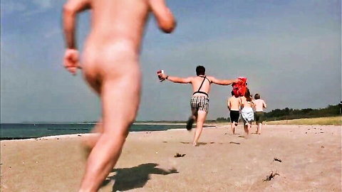 Nude man running on beach exposing bare ass and balls holding red float towards clothed group