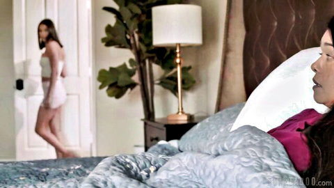 Kylie Rocket lying on bed in purple top as another woman enters room