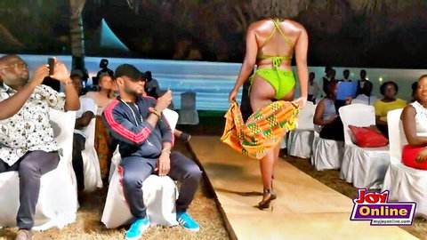 African model struts in green bikini at outdoor fashion show, highlighting curvy booty