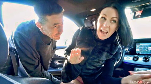 Belinda Bee, mature brunette in fur-trimmed black outfit, teasing in luxury car with man