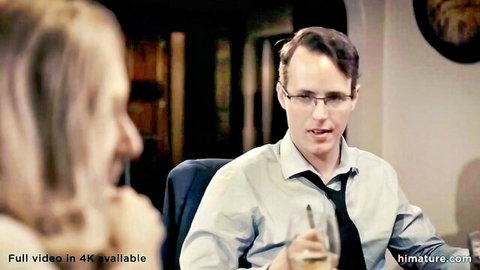 Blonde mature granny seduces suited man with glasses holding wine glass in erotic tease
