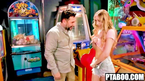 Blonde stepdaughter in pink crop top and denim shorts flirts with stepdad at arcade claw machine