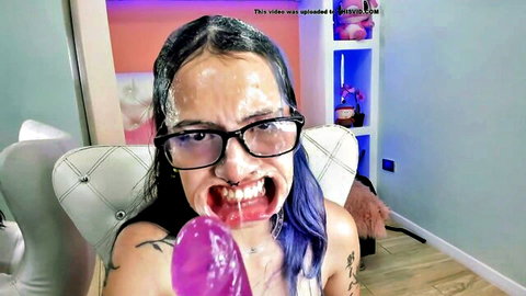 Young purple-haired babe with glasses gets messy cum facial, tongue out holding pink dildo