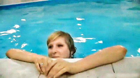 Blonde woman with wet hair resting arms on pool edge smiling teasingly