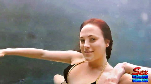 Sexy redhead babe in black bikini swims underwater smiling with wet glistening cleavage and body