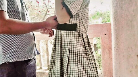 South Asian guy groping young schoolgirl's hips in checkered uniform dress outdoors on balcony