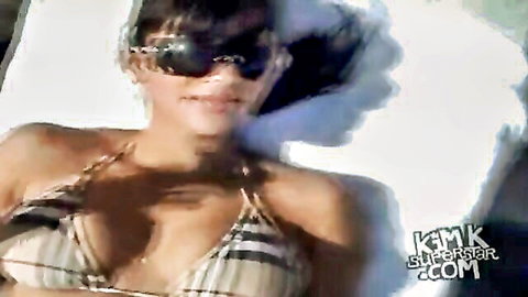 Kim Kardashian lounging in striped bikini, sunglasses on, sexy poolside pose