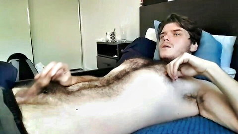 Hairy Kylowe lying shirtless on bed, hand teasing bulge in pants
