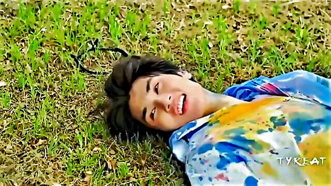 Handsome smiling young Asian man lying on green grass in colorful tie-dye hoodie