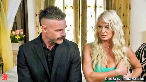 Blonde MILF with huge tits sits with suited man in BDSM bedroom scene