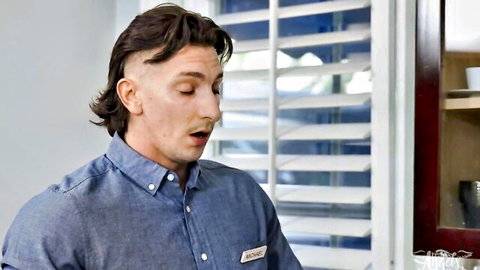 Mullet hairstyle man in blue button-up shirt speaking in kitchen with blinds background