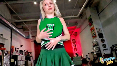 Blonde cheerleader babe in green uniform teases with hands on skirt showing natural tits cleavage