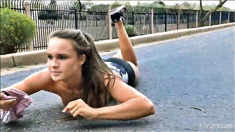 Topless brunette babe with perky tits lying on outdoor road in shorts and sneakers