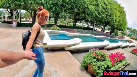 Red-haired Thai girlfriend in jeans and tank top holding hands by fountain, bubble booty tease