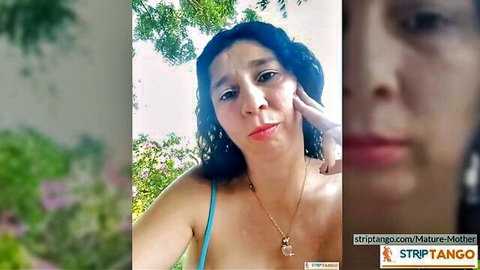 Mature woman with dark wavy hair in blue tank top, sexy outdoor pose
