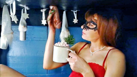 Masked redhead in sexy red lace lingerie holds hot cocoa under hanging Christmas dildo stockings