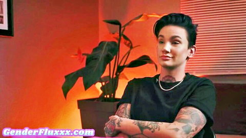 Tattooed androgynous babe with choker smirks arms crossed in warm lit room