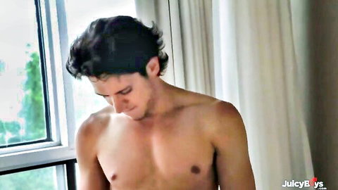 Handsome shirtless curly-haired hunk flexing muscles by window