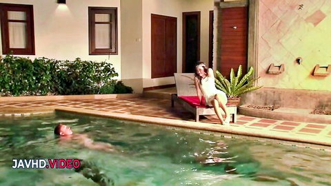 Seductive woman in white bikini lounges poolside with legs spread as man swims in pool