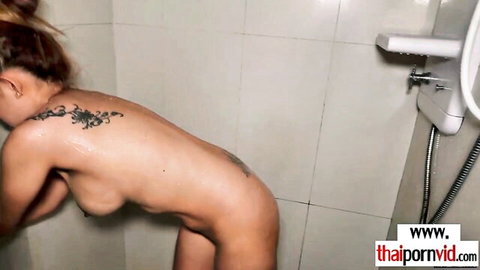 Naked Thai woman with floral tattoos showering, wet curves after workout