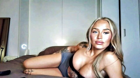 Tattooed blonde babe in sheer lingerie teasing perky nipples on webcam bed