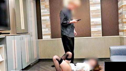 Dominant man stands over submissive Asian woman on floor with legs spread wide in black stockings exposing shaved pussy