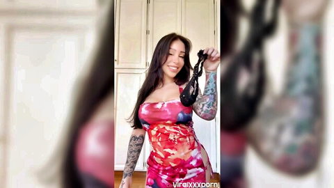 Curvy tattooed brunette with big fake tits holds black panties teasing in skimpy pink dress