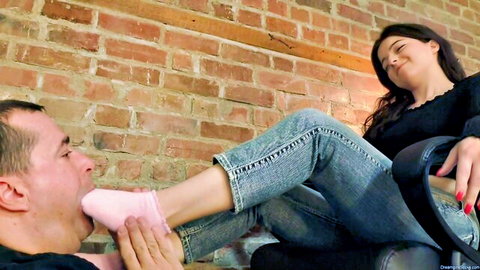 Man sucks on woman's pink socked foot in foot worship fetish while she smiles in jeans