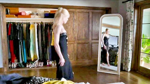 Sexy blonde in strapless black dress admiring reflection in mirror in luxurious bedroom closet