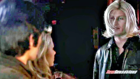 Blonde guy in leather jacket facing sexy blonde woman in dim bar setting