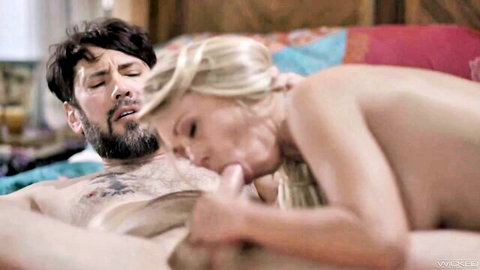 Blonde nude MILF sucking bearded man's thick cock passionately on colorful bed