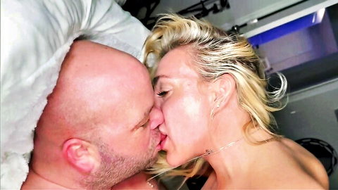 Nude blonde MILF with big tits passionately kissing bald bearded man on bed