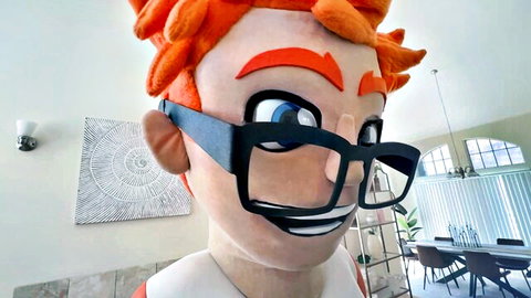 Cheerful cartoon mascot with orange spiky hair and black glasses smiling in modern living room
