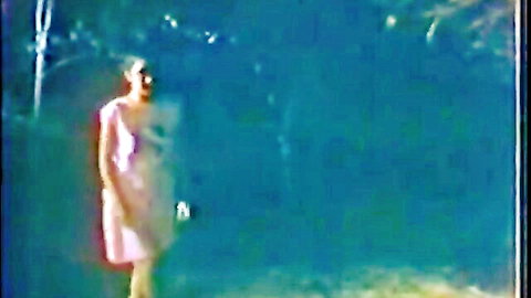 Vintage 1986 Asian woman in short pink dress standing by poolside